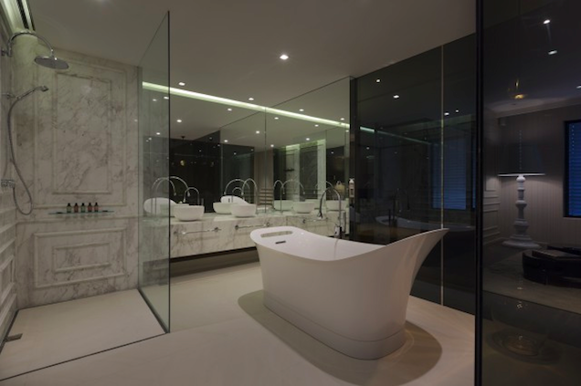 Bathroom With Glass Walls, Architectural White Bathtub, and Striated Marble Vanity Cabinets